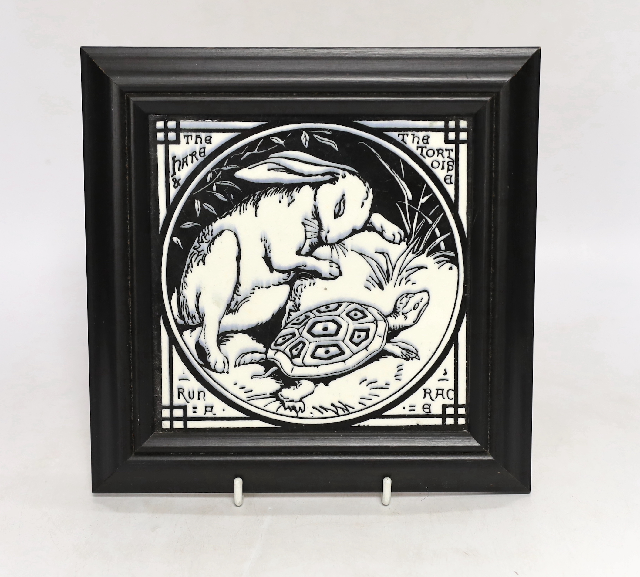 A framed Arts and Crafts Aesops Fable Minton monochrome tile “The Hare and the Tortoise run a race”, 21cm x 21cm including frame